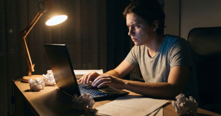 Beginner writer experiencing writer’s block at desk with crumpled drafts symbolizing creative struggle