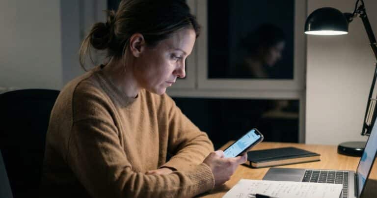 AI-generated caption performance drop, course creator checking low engagement on phone in home office at night