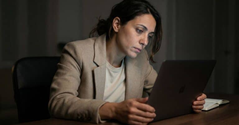 AI content creator editing blog post at night, laptop screen reflecting editing fatigue in home office