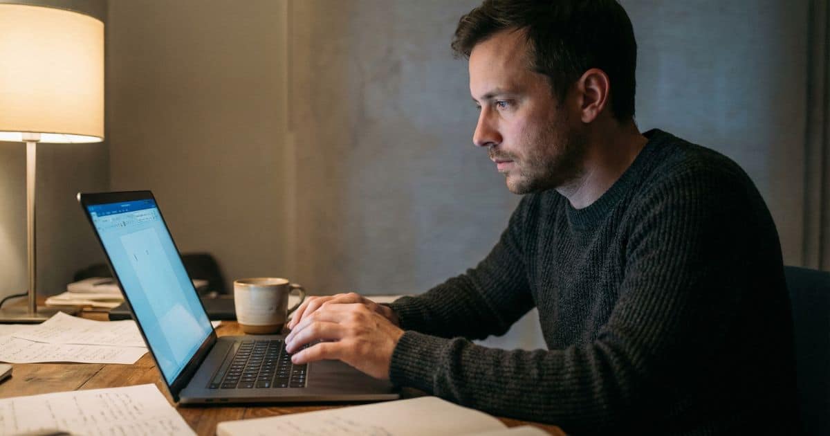 creative block at night, male writer staring at blank laptop screen in dim home office with cold coffee mug