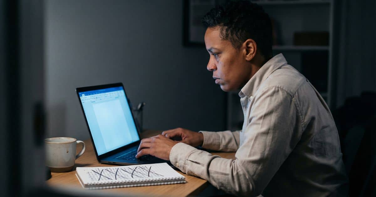 Writer deleting novel draft at 2 AM in dim home office, laptop glow lighting tense expression and crossed-out notebook.